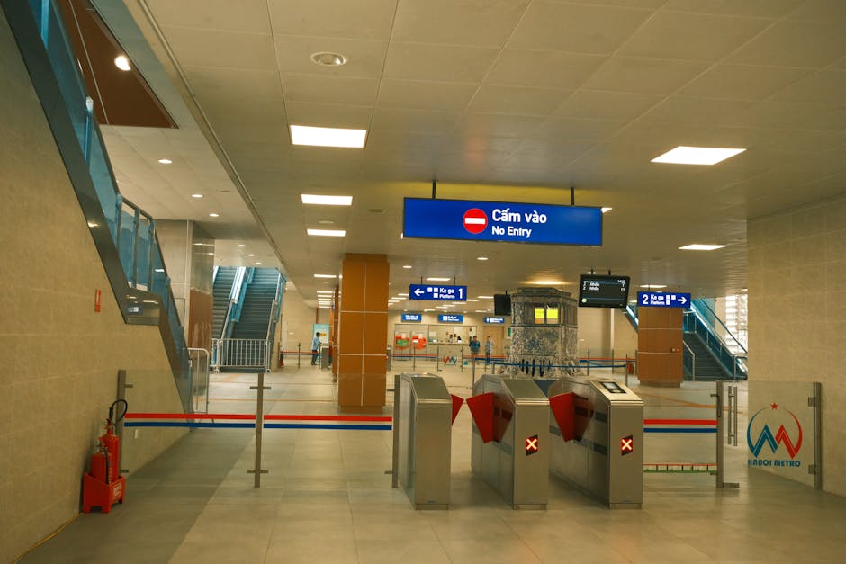 Image of passengers disembarking from a red and white London Underground train inside an curved underground station tunnel with a tiled ceiling and modern lighting. Several individuals are walking along the platform, some carrying luggage or backpacks, while others are descending a staircase towards the station's upper level. The platform surface features tactile paving strips and yellow safety lines, indicating a busy transit environment. The scene depicts a typical morning or daytime commute, with people transitioning between train and station access points. This setting exemplifies the logistical environment encountered during property or furniture transport, involving careful movement and handling of belongings in an urban public transport context, relevant to home relocation or removals.